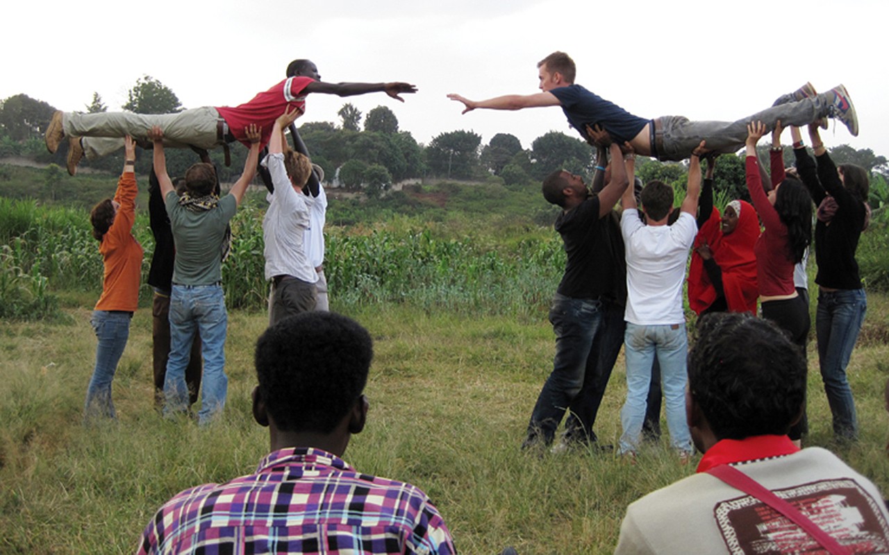 Two students reach toward each other as they are lifted in the air by their classmates in a field in Kenya