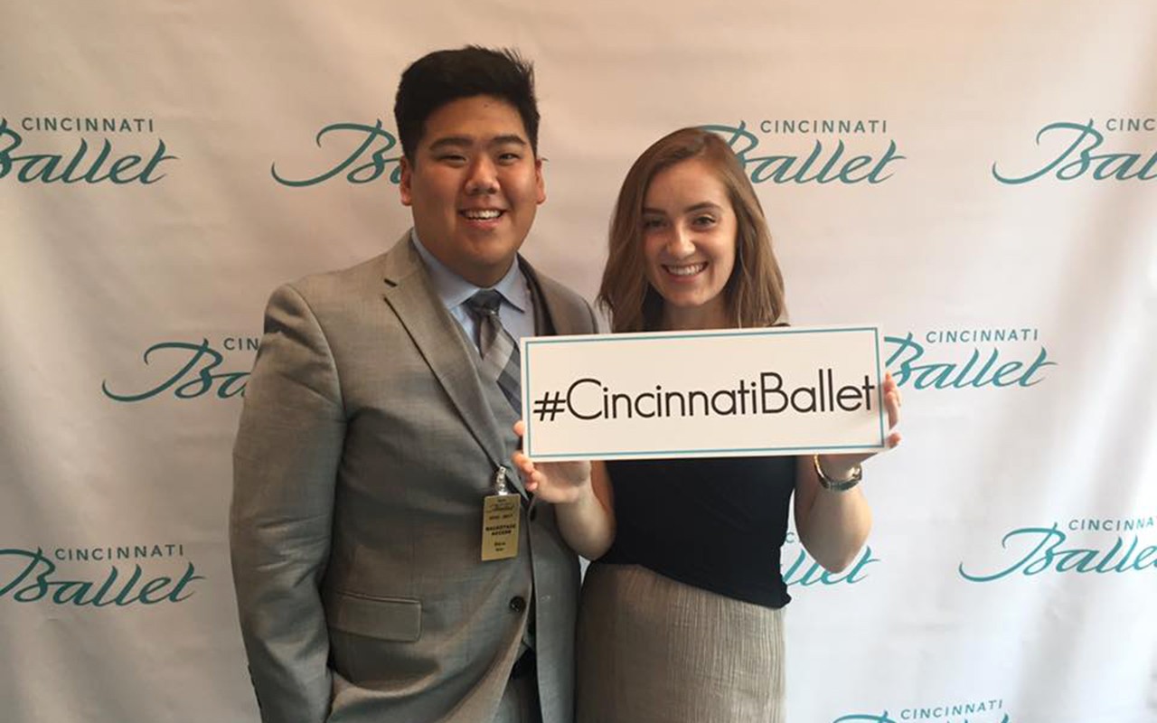 Two Arts Administration students pose in front of a Cincinnati Ballet backdrop holding a sign reading #CincinnatiBallet