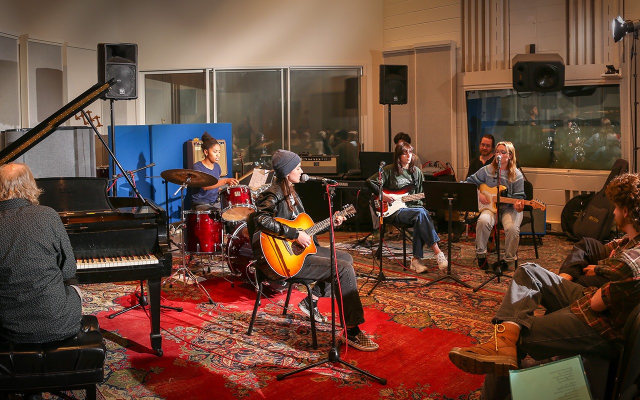 Commercial Music Production students perform on guitar, drums and piano for an audience.
