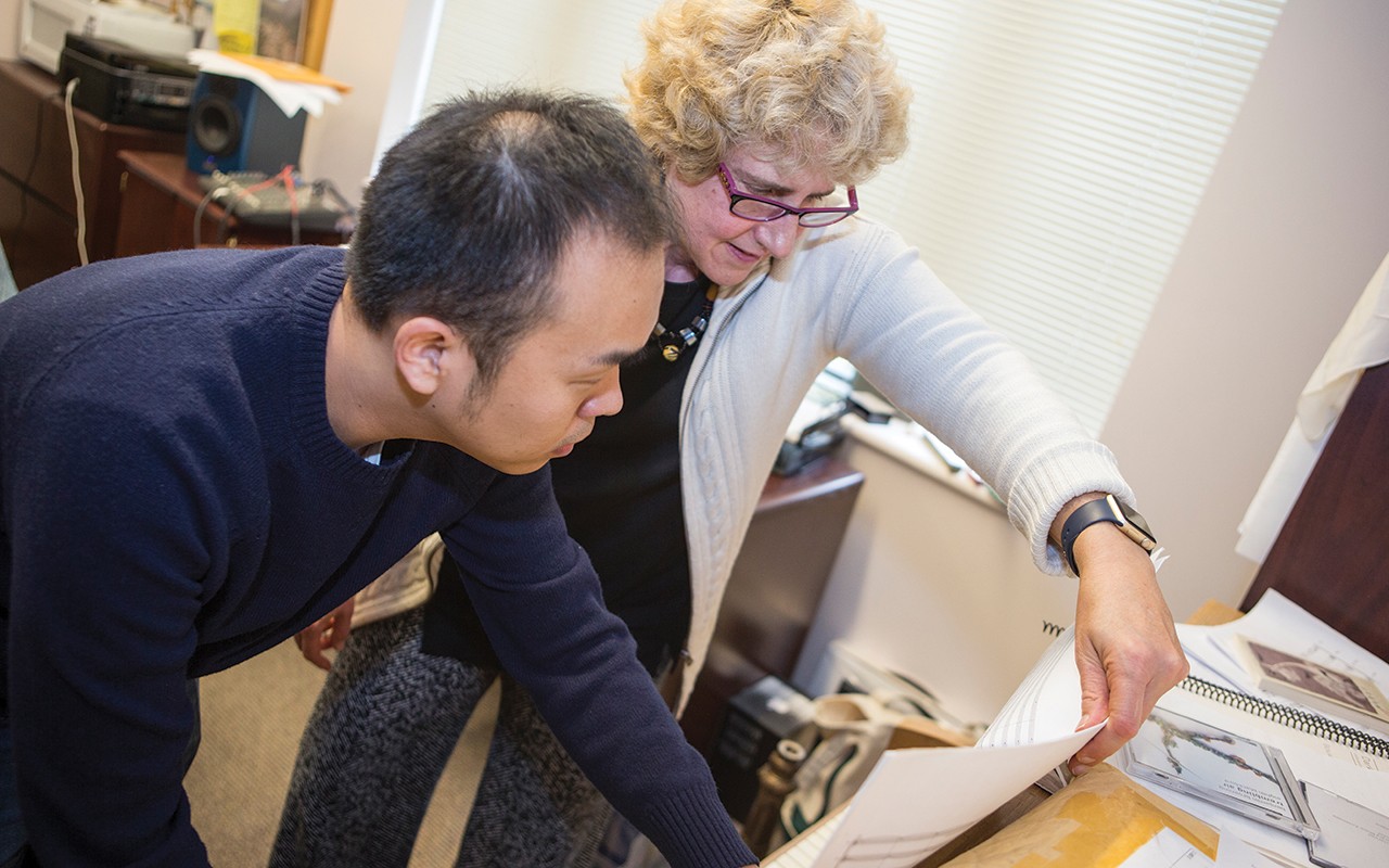 Composition professor reviews sheet music on a piano with her student