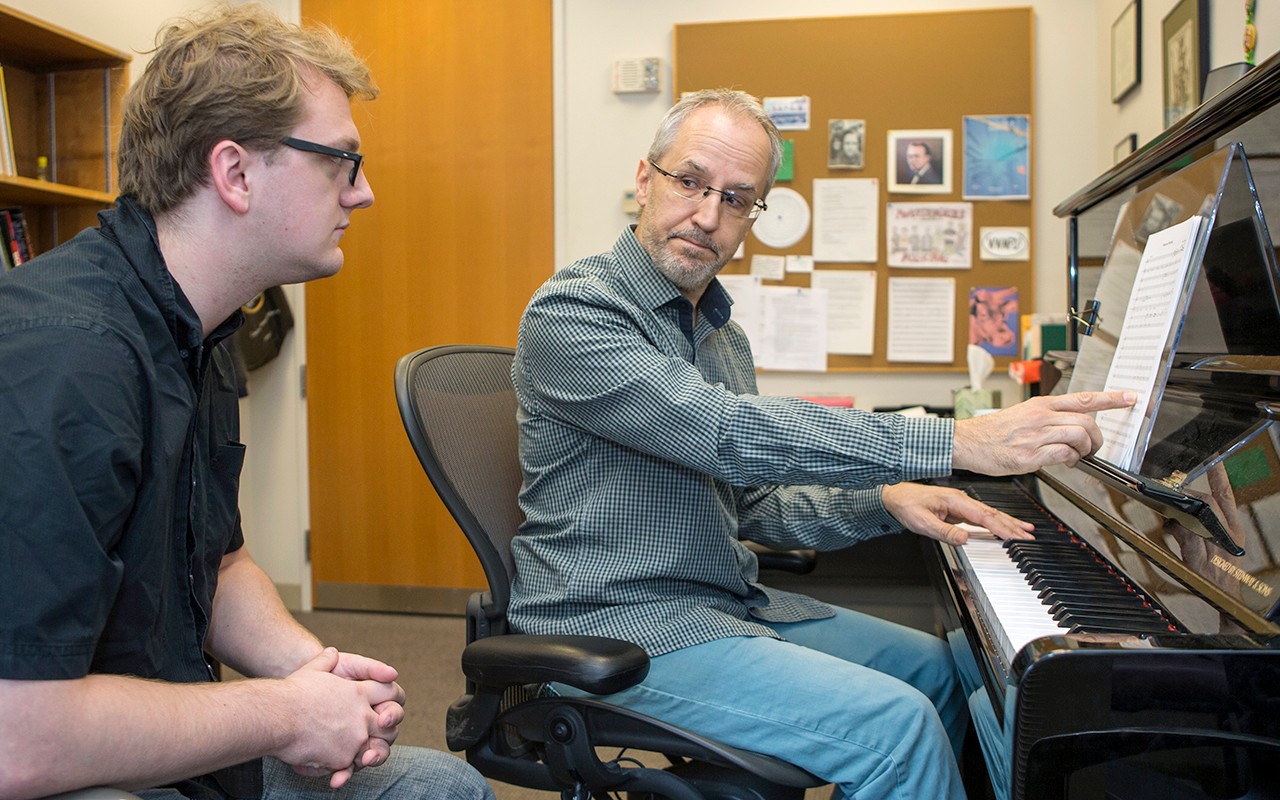 Composition faculty member reviews a piece of sheet music with a student while sitting at a piano