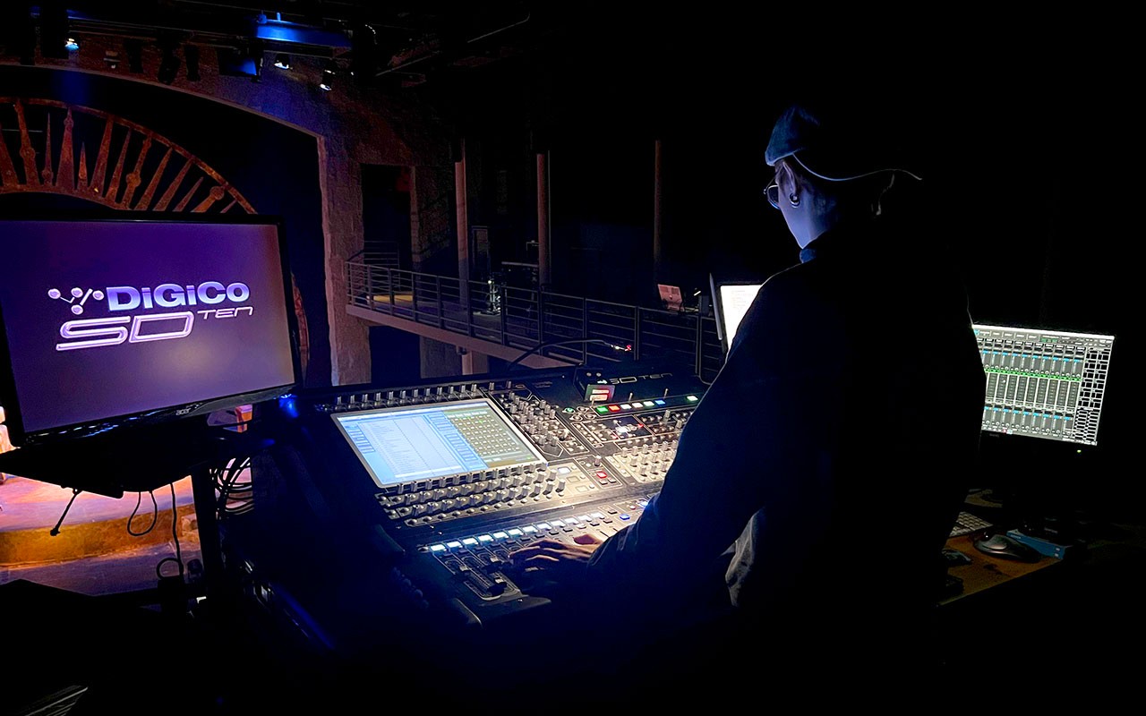 Sound Design student sits at control panel monitoring multiple glowing monitors