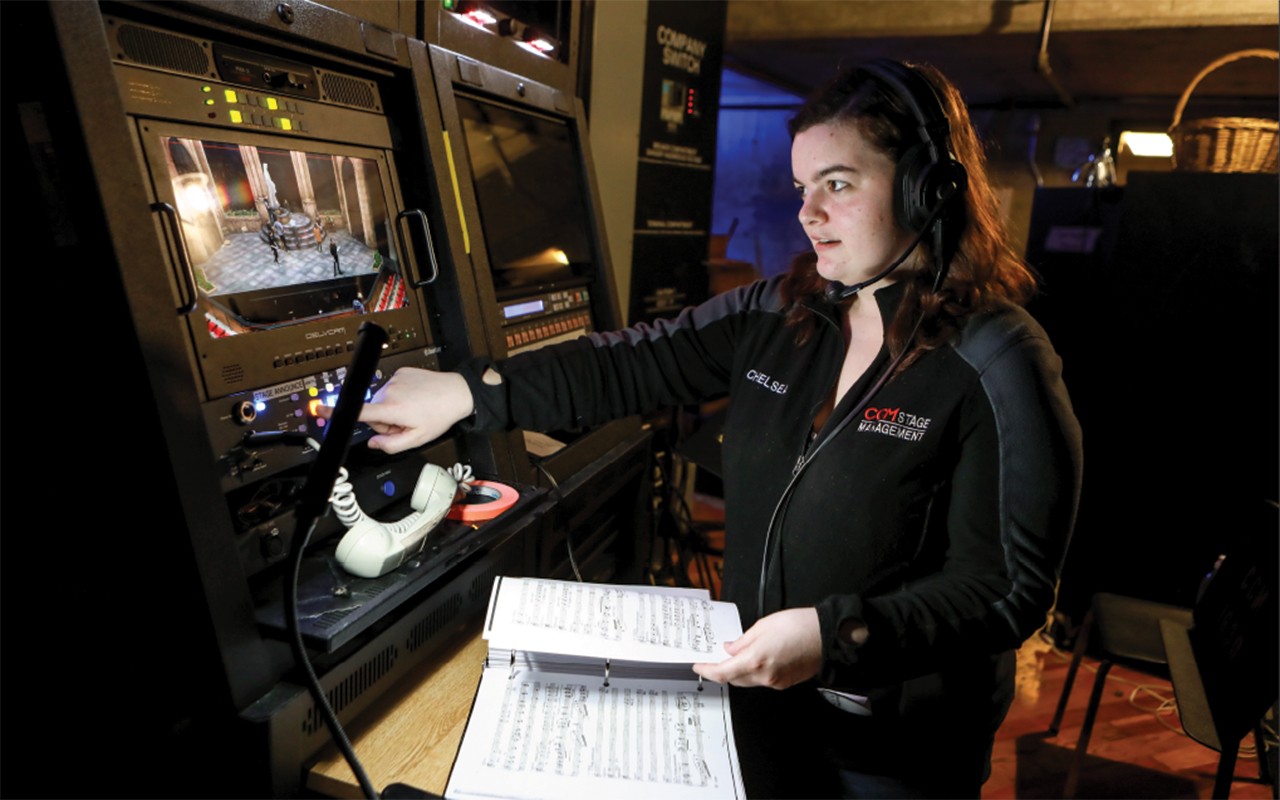Stage Management student stands backstage consulting a video screeen and music score