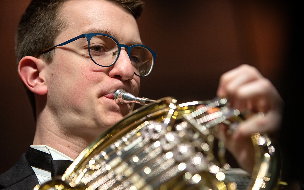 Male french horn student performs with the concert orchestra in Corbett Auditorium